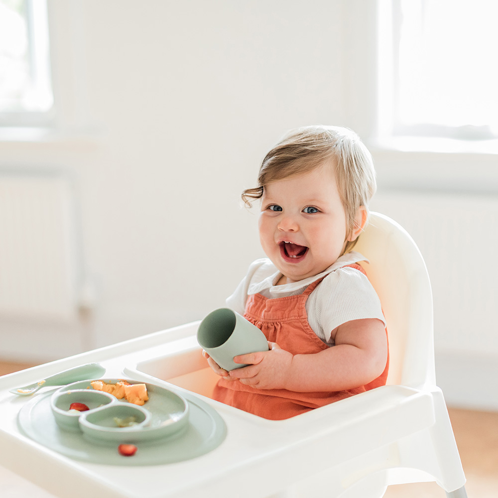 little smiling girl having lunch in a highchair using ezpz feeding products in sage