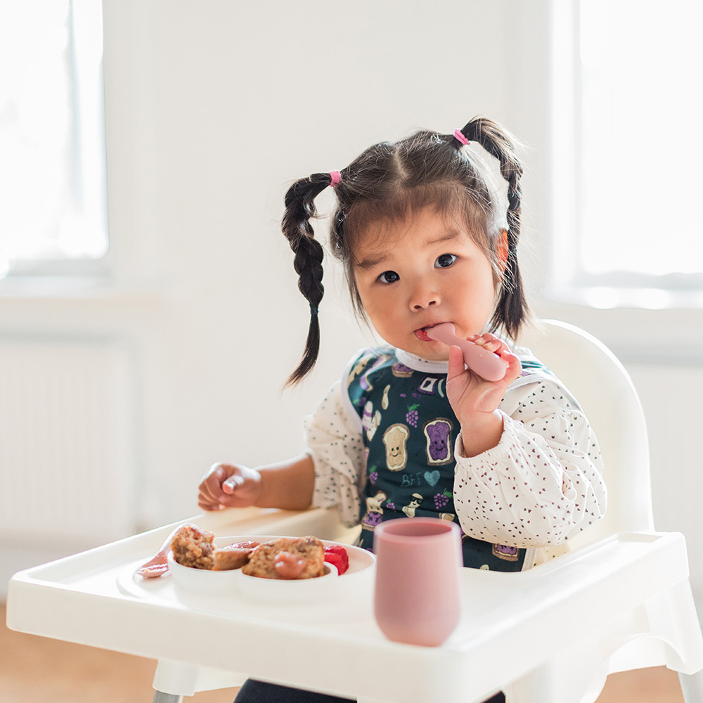 Canadian girl eating with an ezpz Mini Spoon and wearing a BapronBaby bib