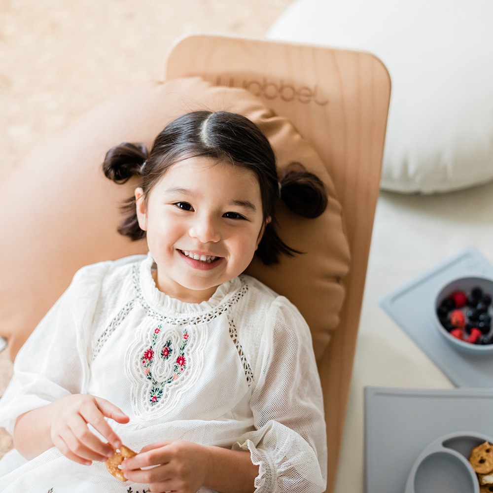little girl leaning on a wobbelboard eating berries from an ezpz mini bowl