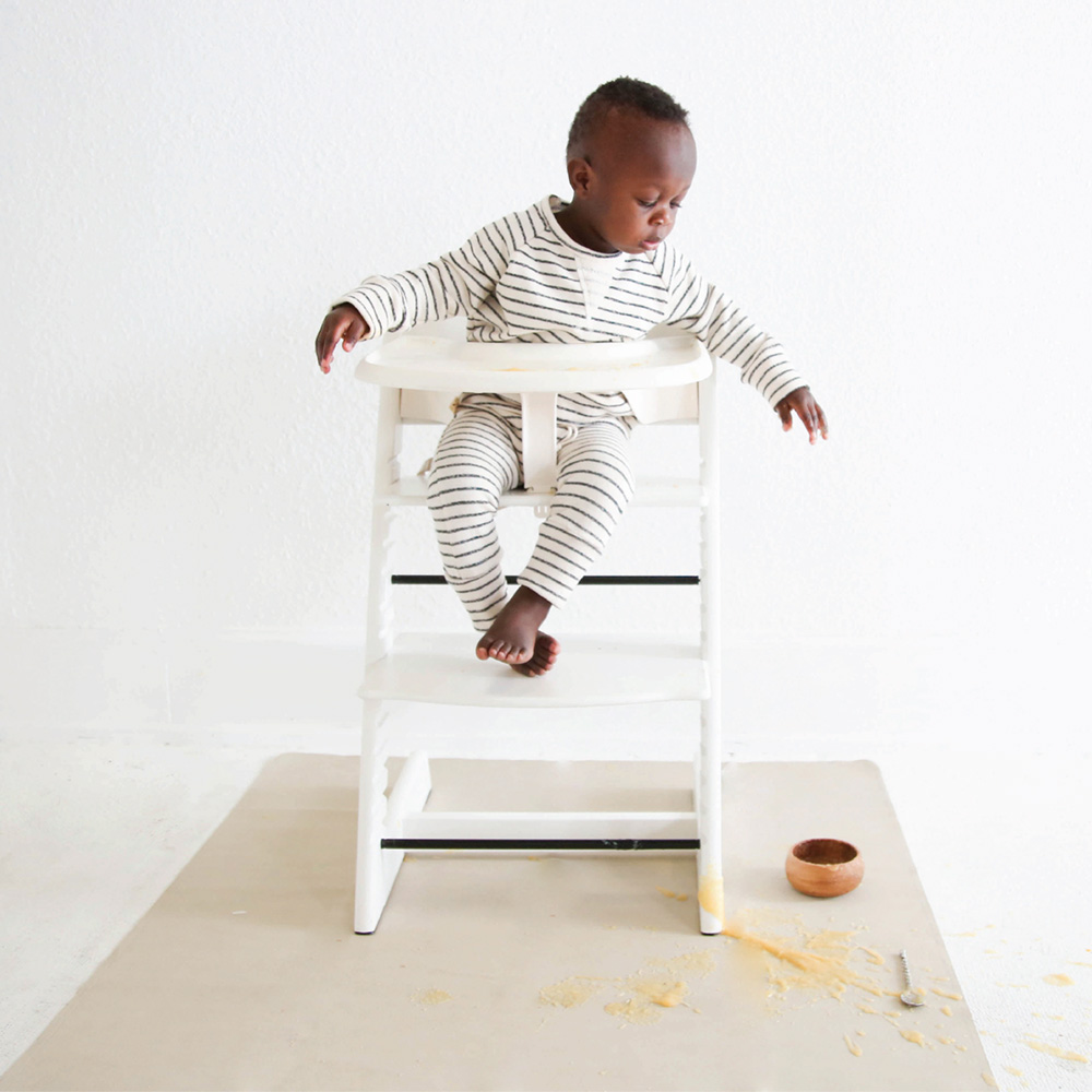 baby dropping food from a highchair with a Gathre mini mat on the floor below him