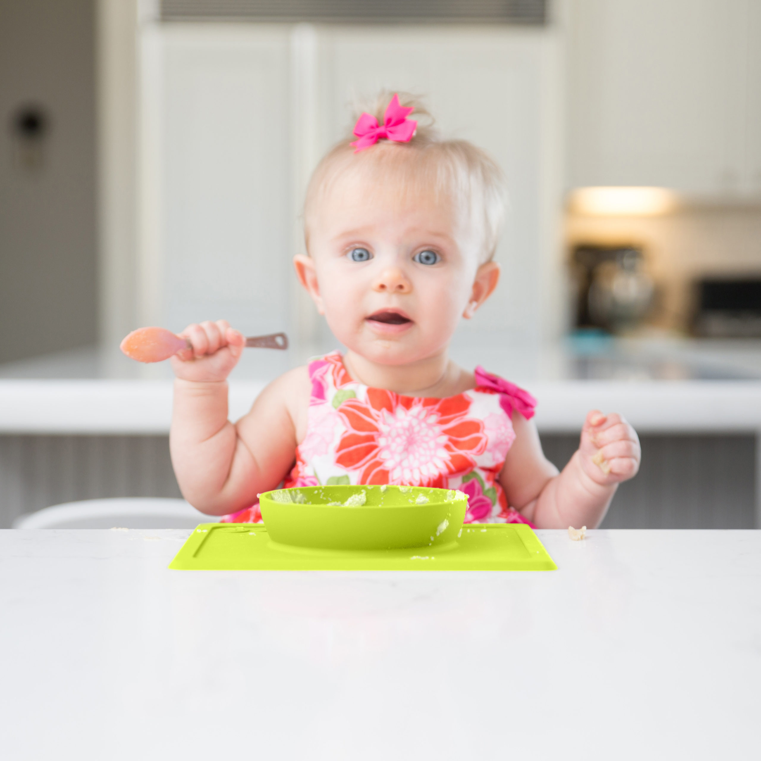little girl clutching a spoon, eating from an ezpz mini bowl in lime