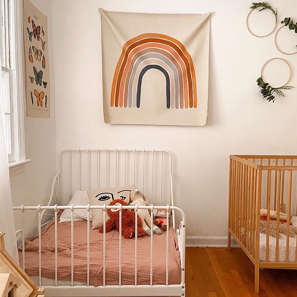 a modern children's bedroom with a Gathre rainbow tapestry hanging above the bed